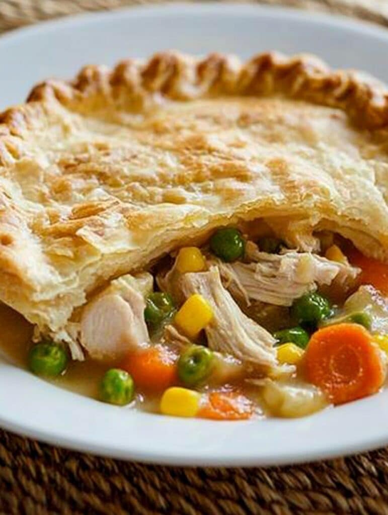 A golden, flaky chicken pot pie with a crispy crust, filled with tender shredded chicken, carrots, peas, and corn in a rich, savory gravy.